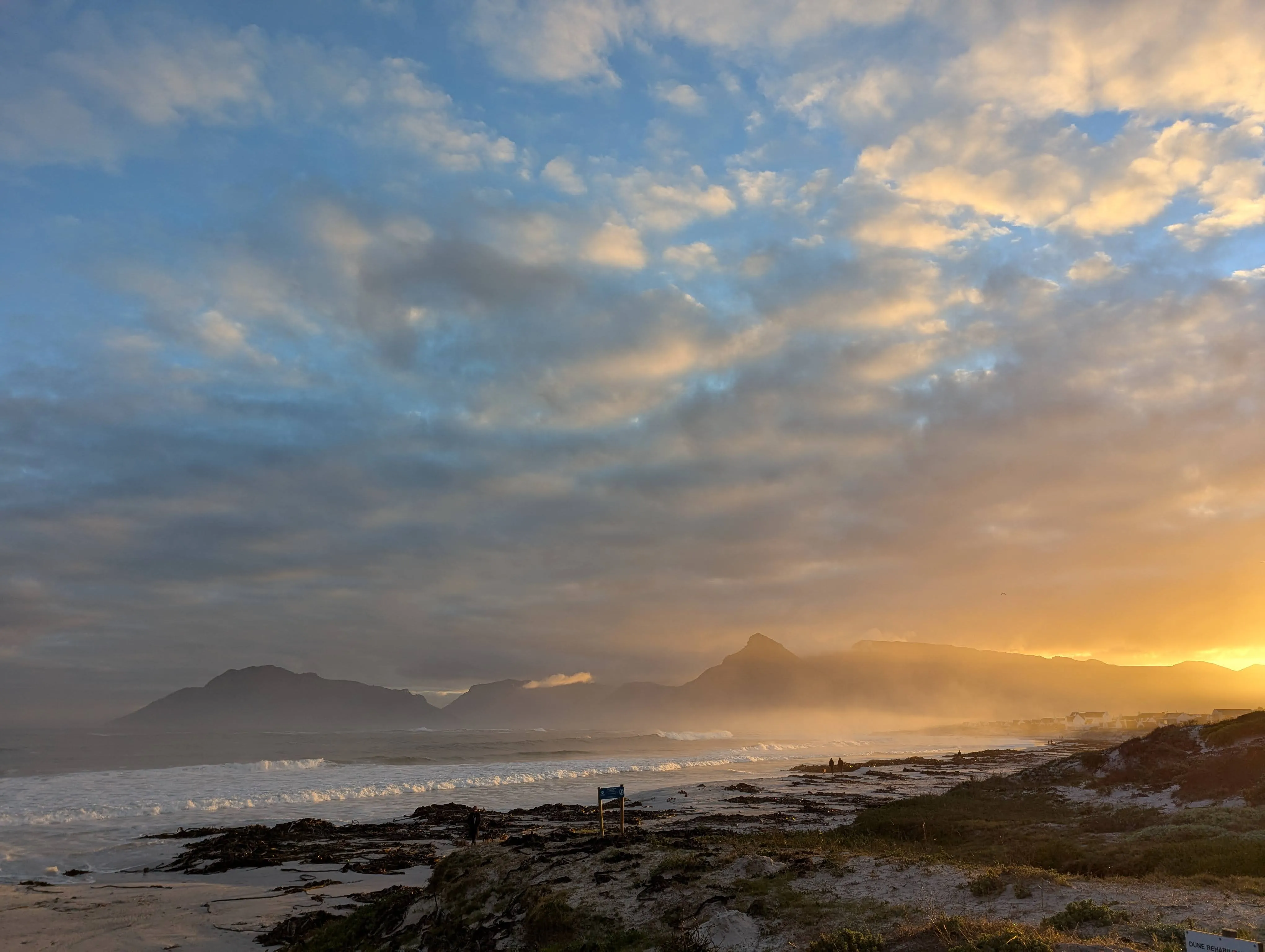 Pale pink and gold sunrise washing over Kommetjie’s beach—quiet, early light.