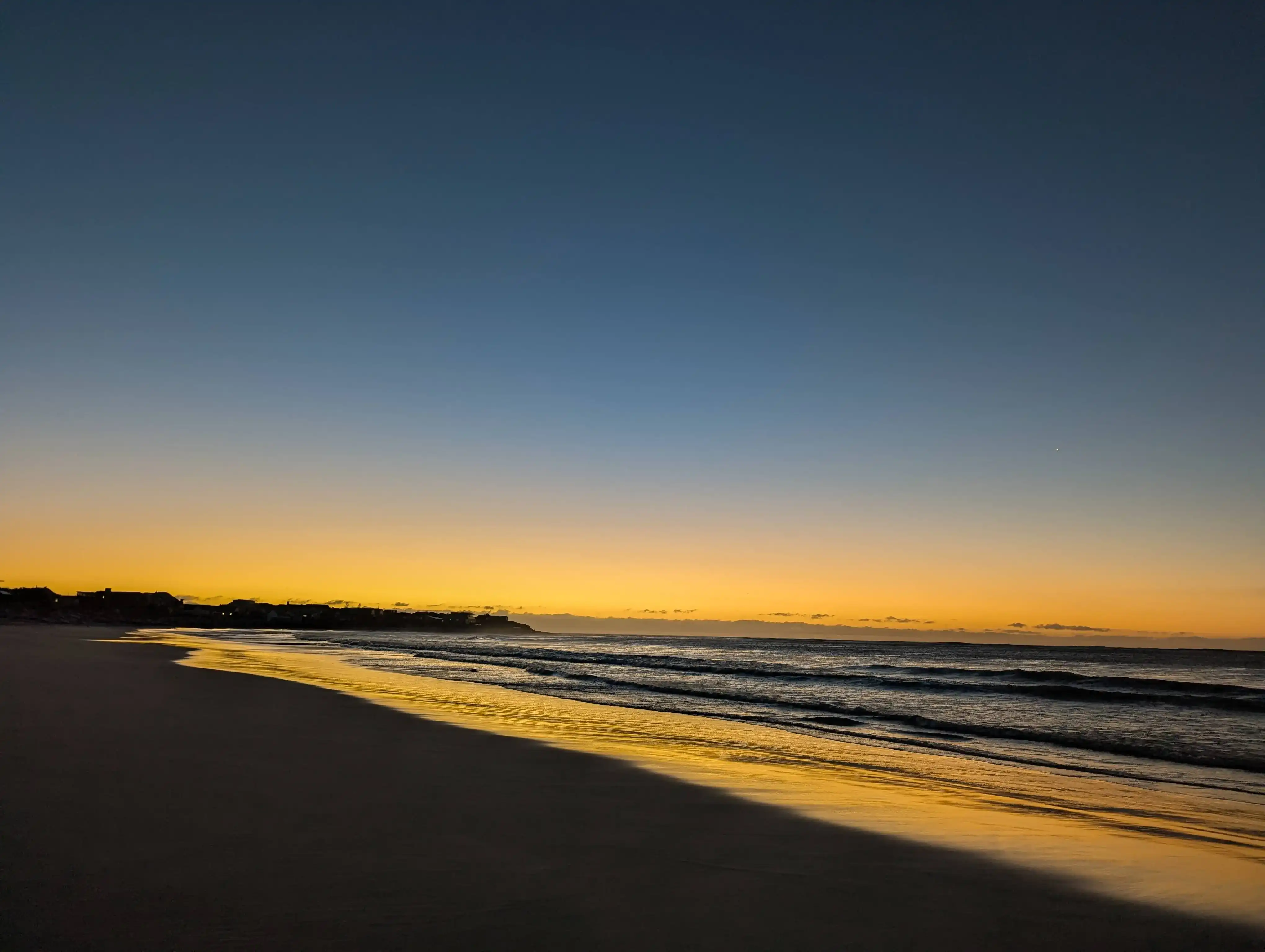 A glowing Kommetjie sunset over Long Beach with warm light reflecting on the water.